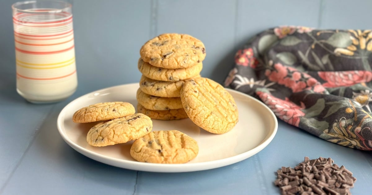 Stack of Biscuits on a white plate with a glass of milk in the background and a pile of chocolate chips in front.