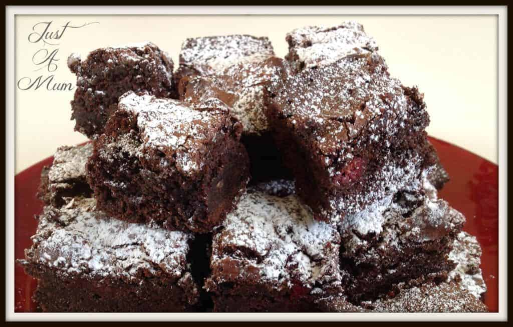 A plate full of chocolate brownie with raspberries dusted in icing sugar on a red plate. 