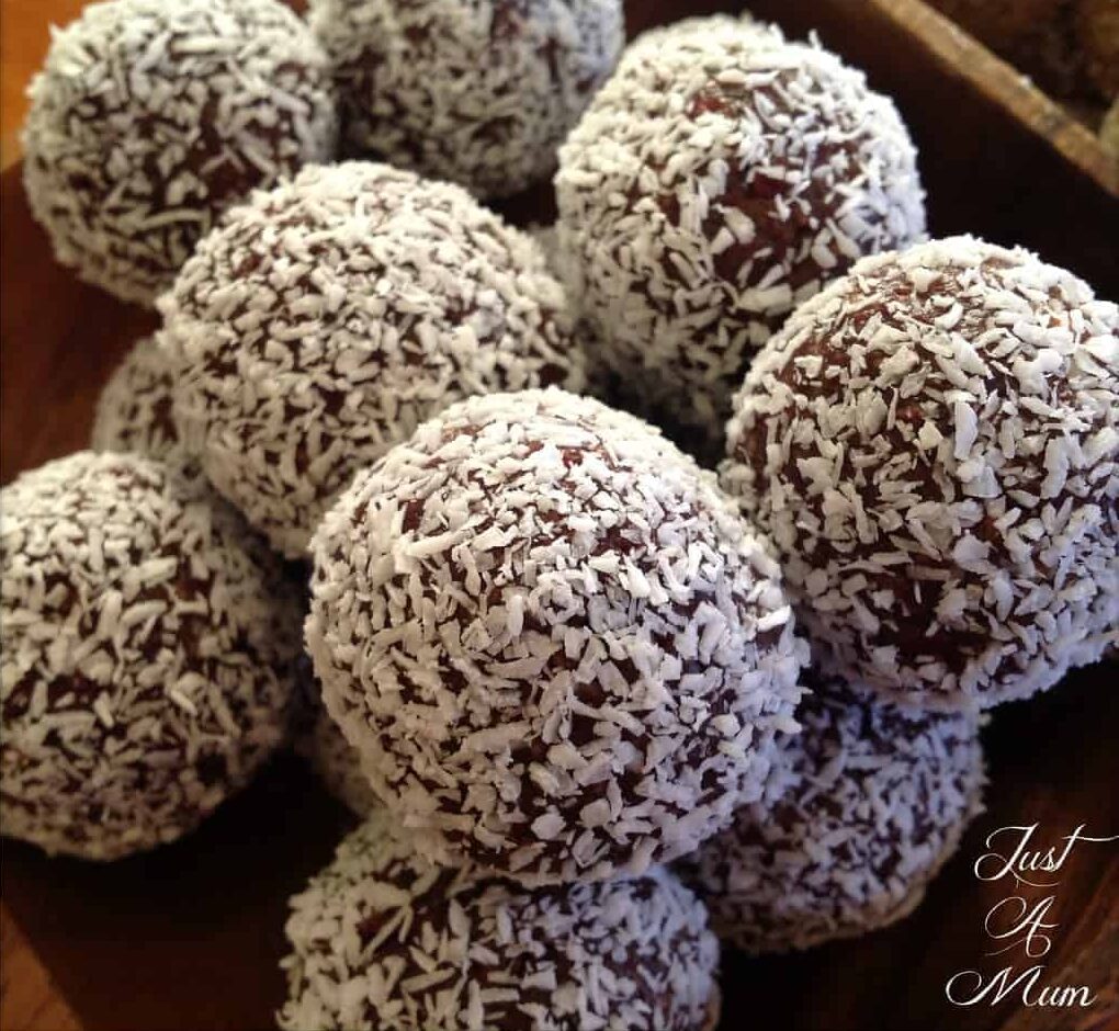 Cranberry Date Cashew Bliss Balls covered coconut in a pile in a wooden bowl