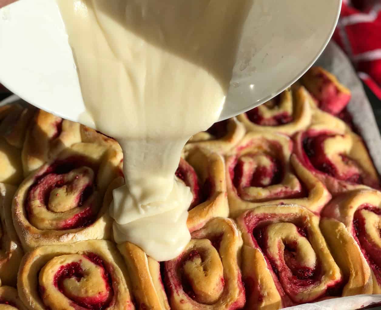 Pouring lemon frosting on soft raspberry lemon rolls