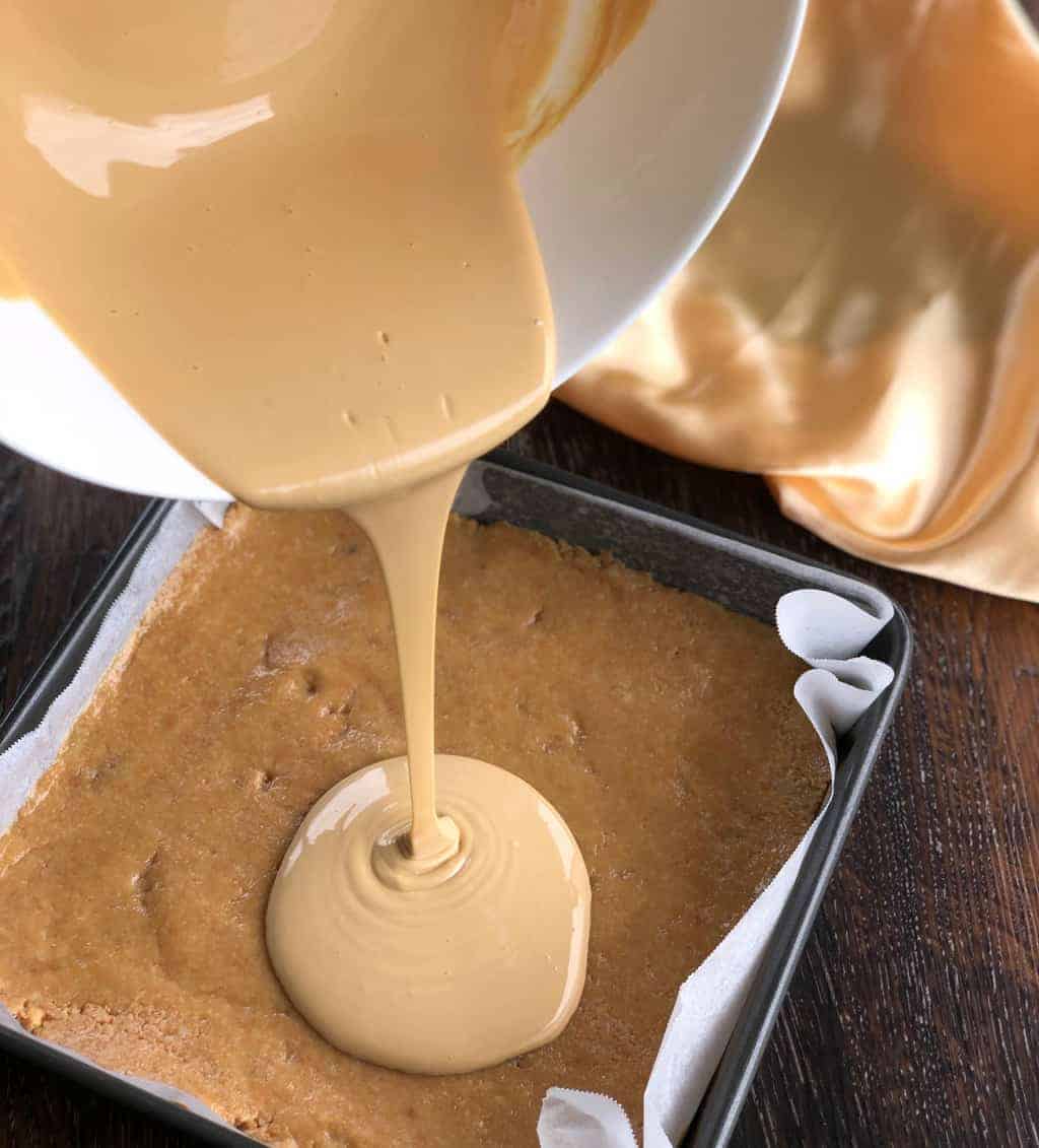 Pouring melted caramilk over a no bake slice