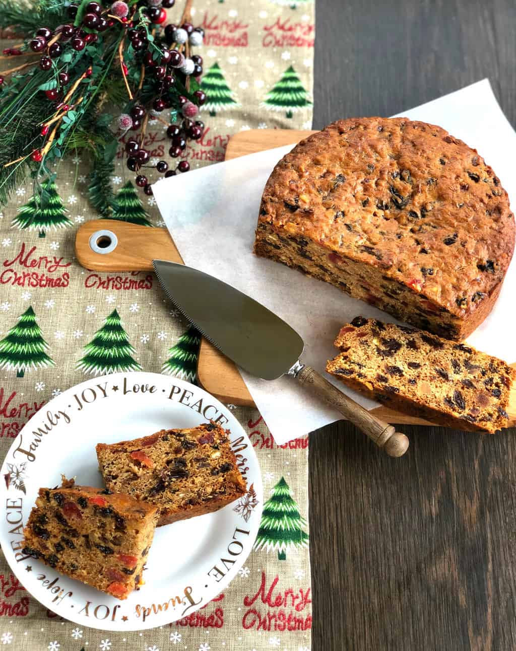 Overhead view of Two slices of Christmas Cake, the rest of the cake and the Christmas branch of berries