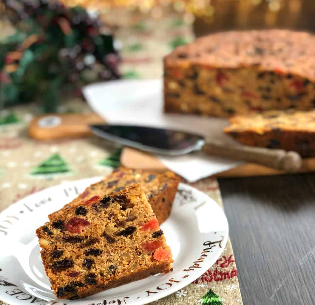 Two Slices of Delicious Christmas Cake with the rest of the cake in the background.