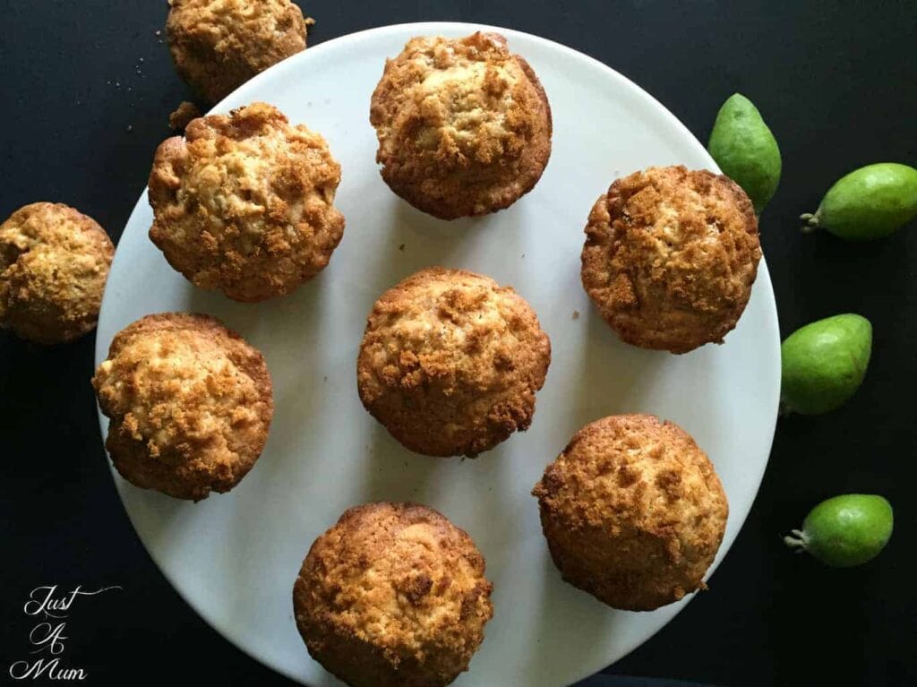 A birds-eye view photo of Just A Mum's Kitchen Feijoa Crunch Muffins served on a cake stand with fresh feijoa in the background.