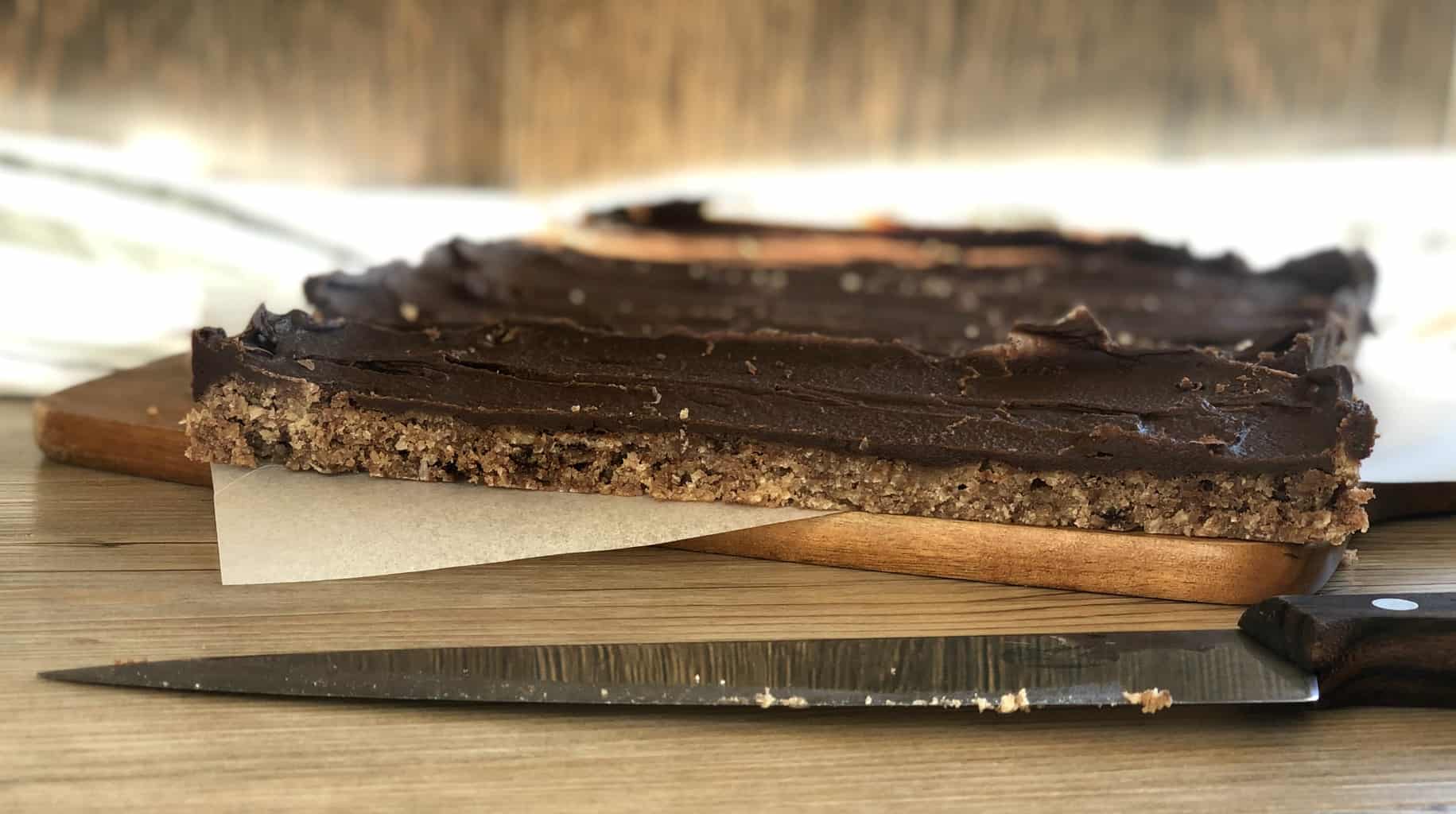 Long slices of a baked and iced chocolate slice with a sharp knife