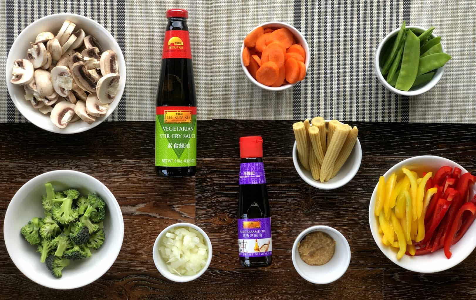 Flatlay of prepared vegetables for Vegetarian Stir Fry, mushrooms, broccoli, onion, garlic, baby corn, carrots, snow peas capsicum and two Lee Kum Kee sauces