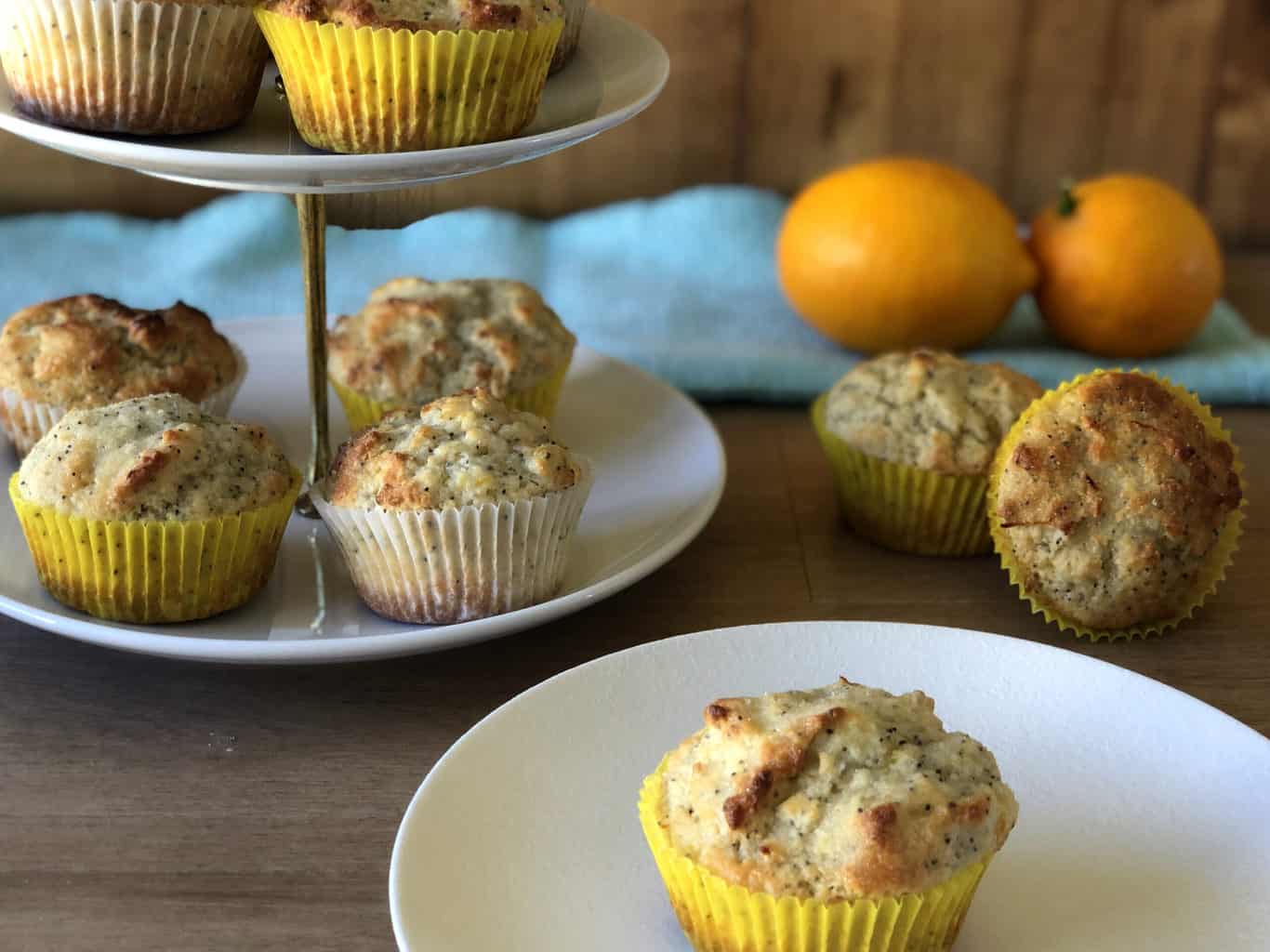 Tiered plate of lemon muffins with two fresh lemons and other muffins scattered around