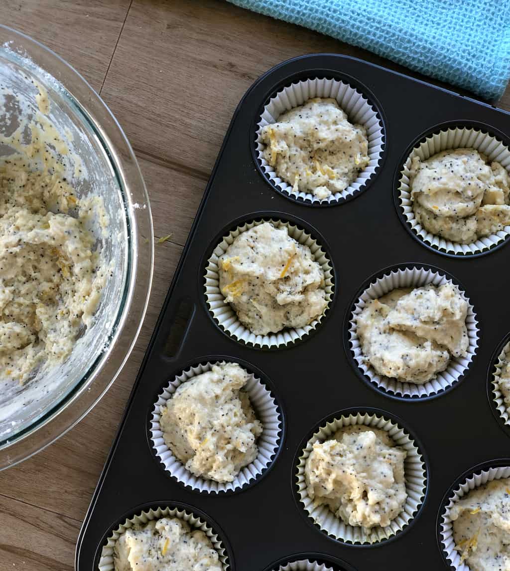 Uncooked batter for lemon and poppy seed muffins in cupcake cases in a black muffin tray. 