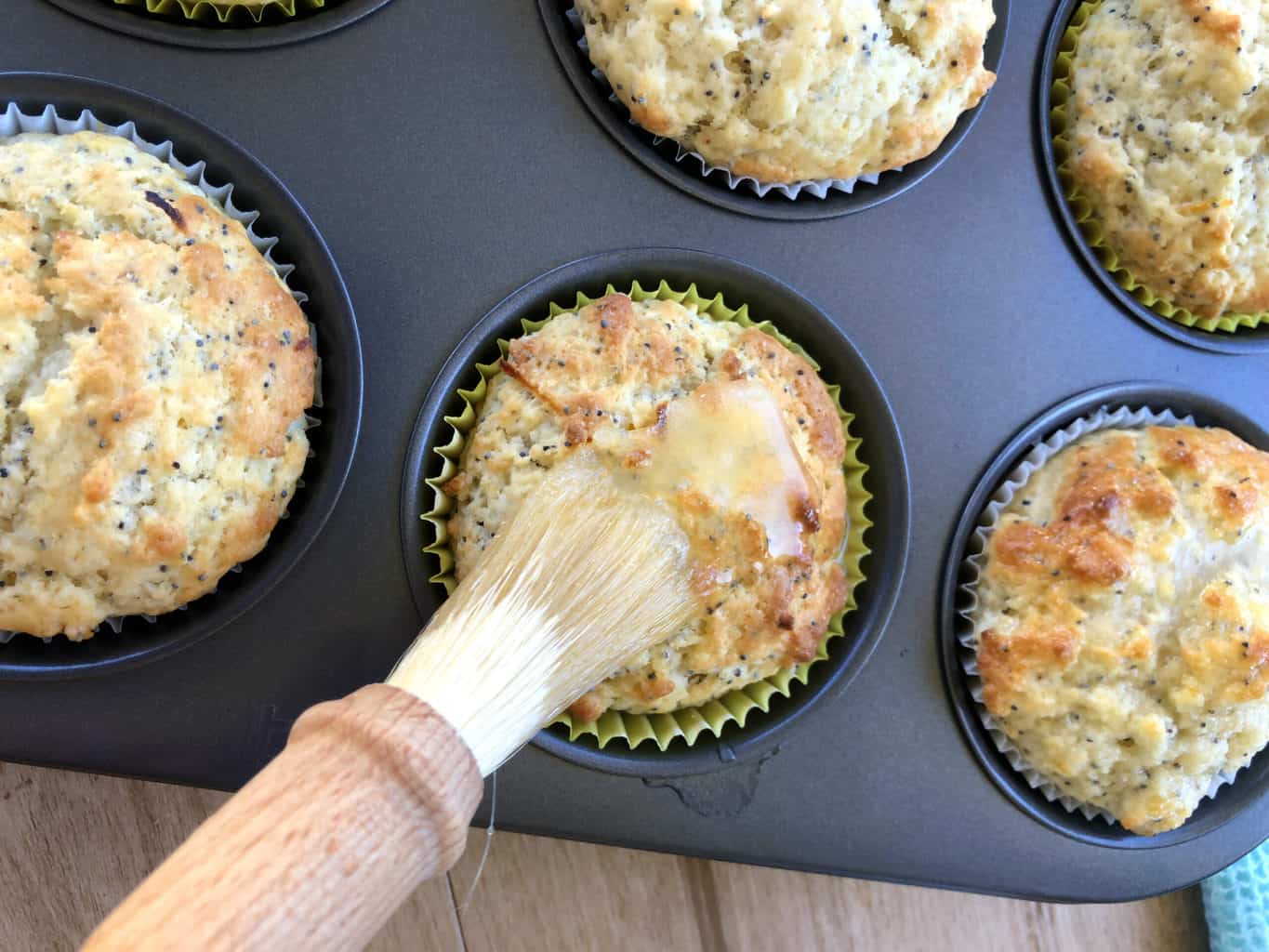 Baked muffins being spread with glaze with a pastry brush