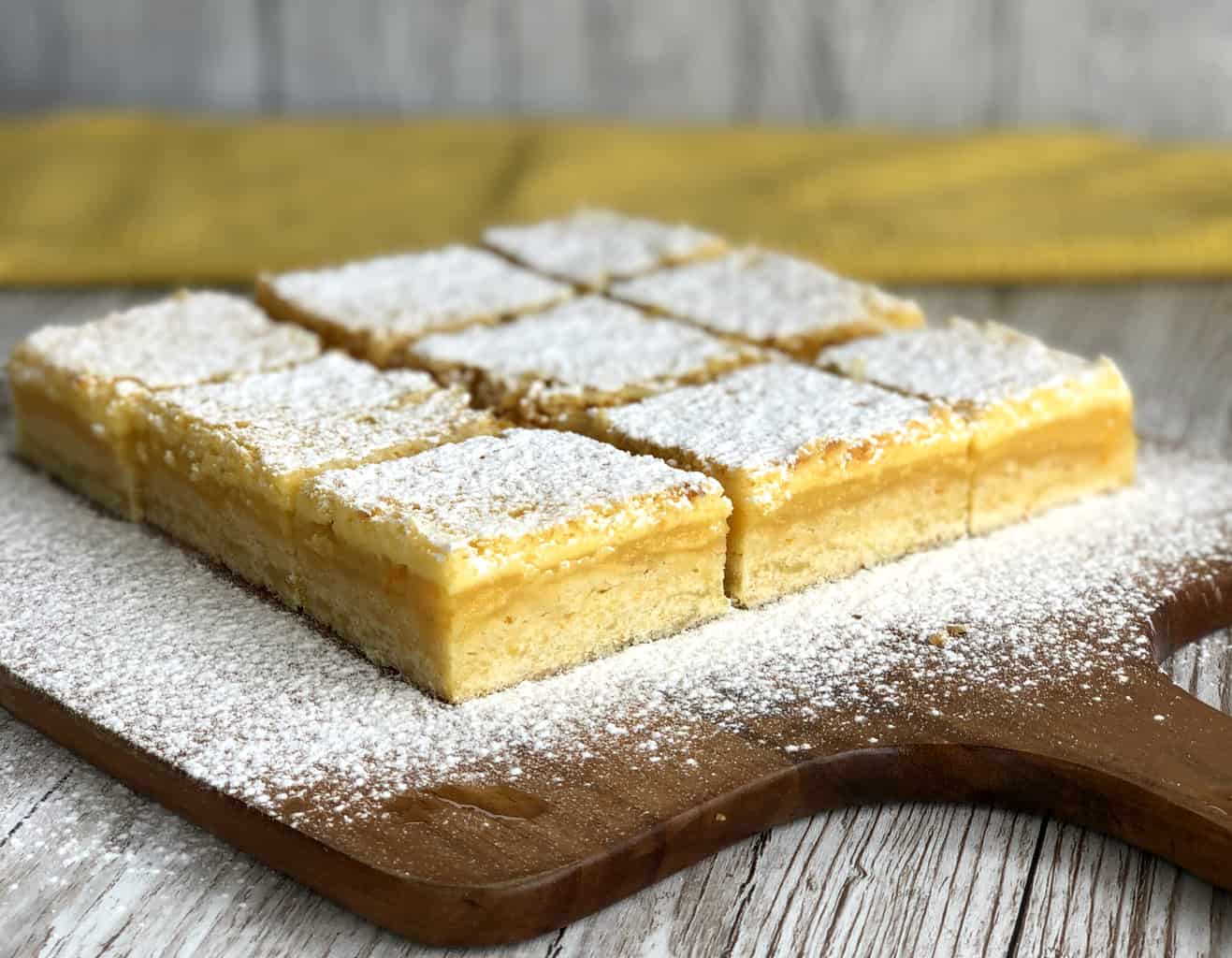 Wooden chopping board with lemon slice cut and dusted with icing sugar on a white table. 