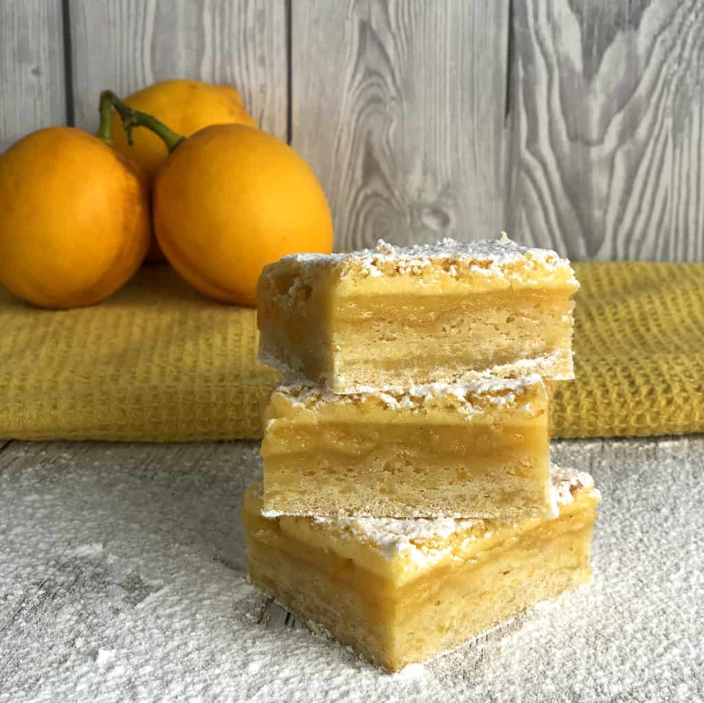 Stack of three slices of lemon squares with lemons in the background on a white table 