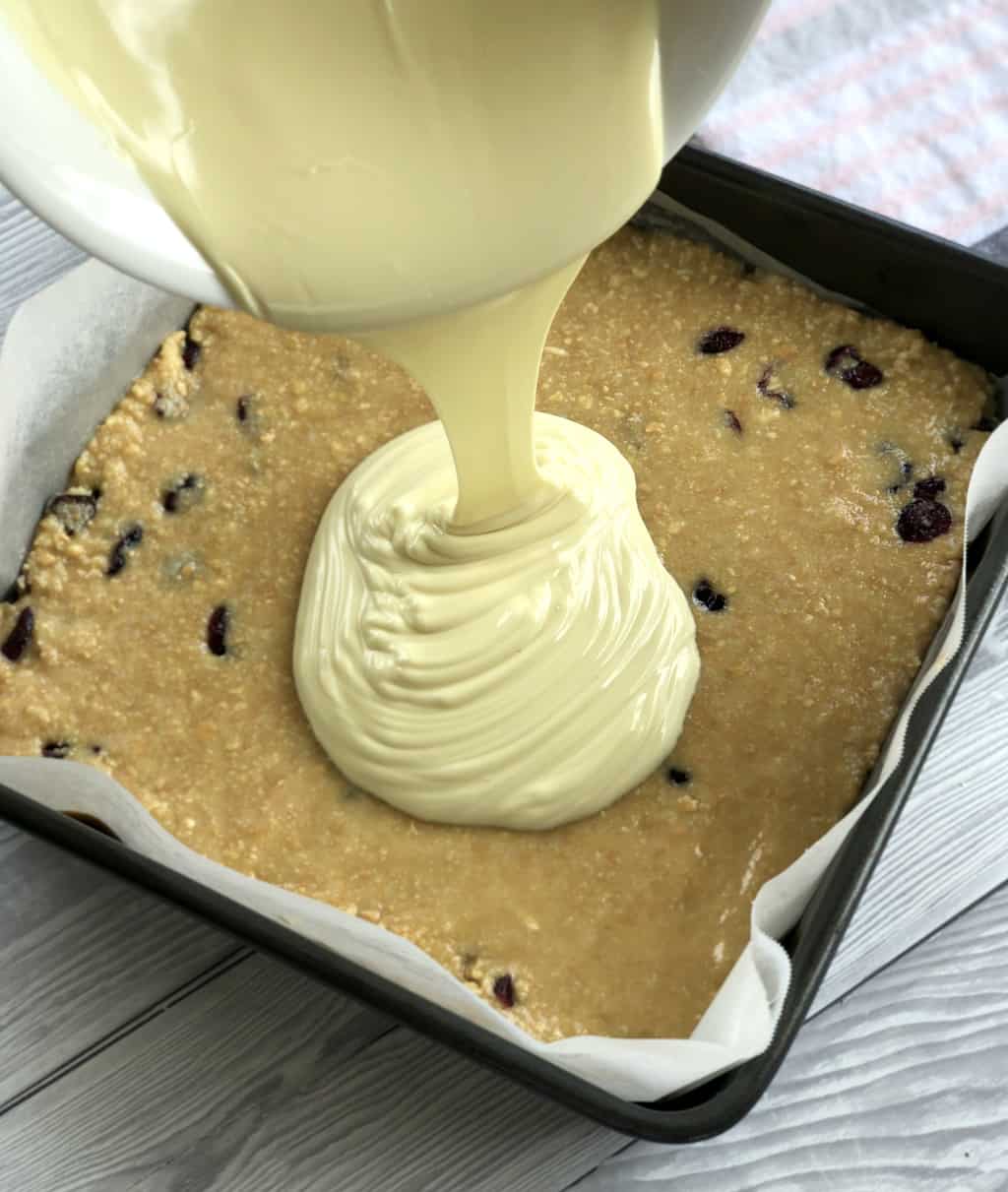 Pouring white chocolate over the cranberry white chocolate no bake slice 