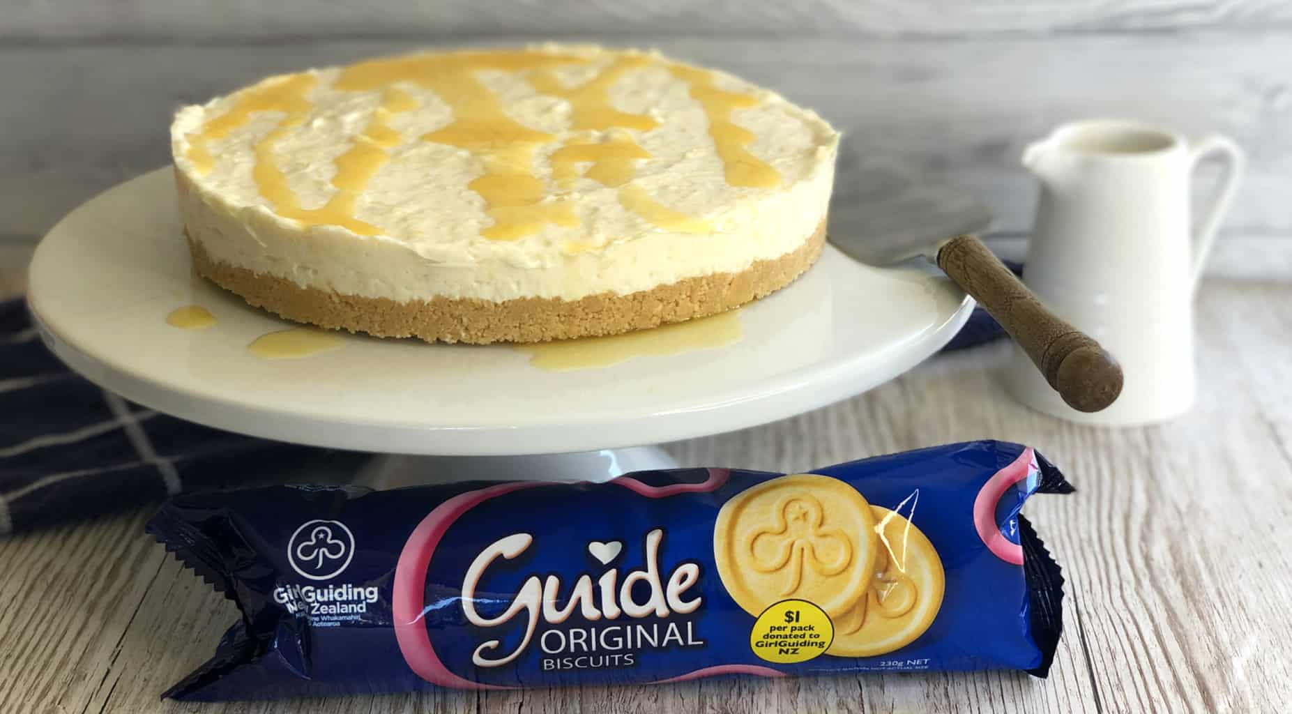 Whole Pineapple Cheesecake on a white cake stand and a packet of Girl Guide Biscuits 