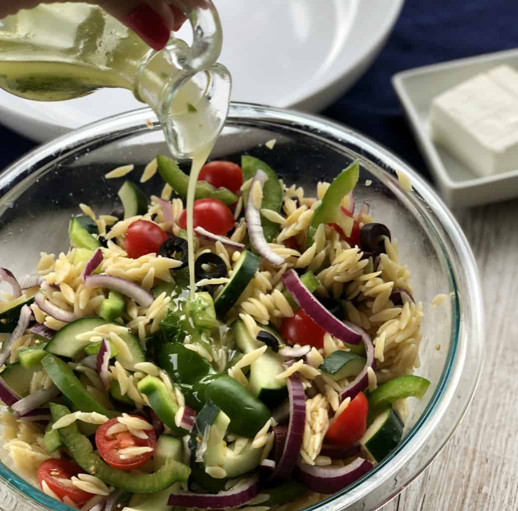 Pouring Greek Salad Dressing over a Orzo Pasta Salad. 