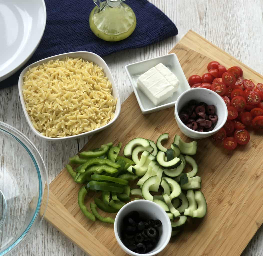 Prepared ingredients for the Greek Orzo Salad, sliced vegetables, dressing and pre cooked orzo pasta. 