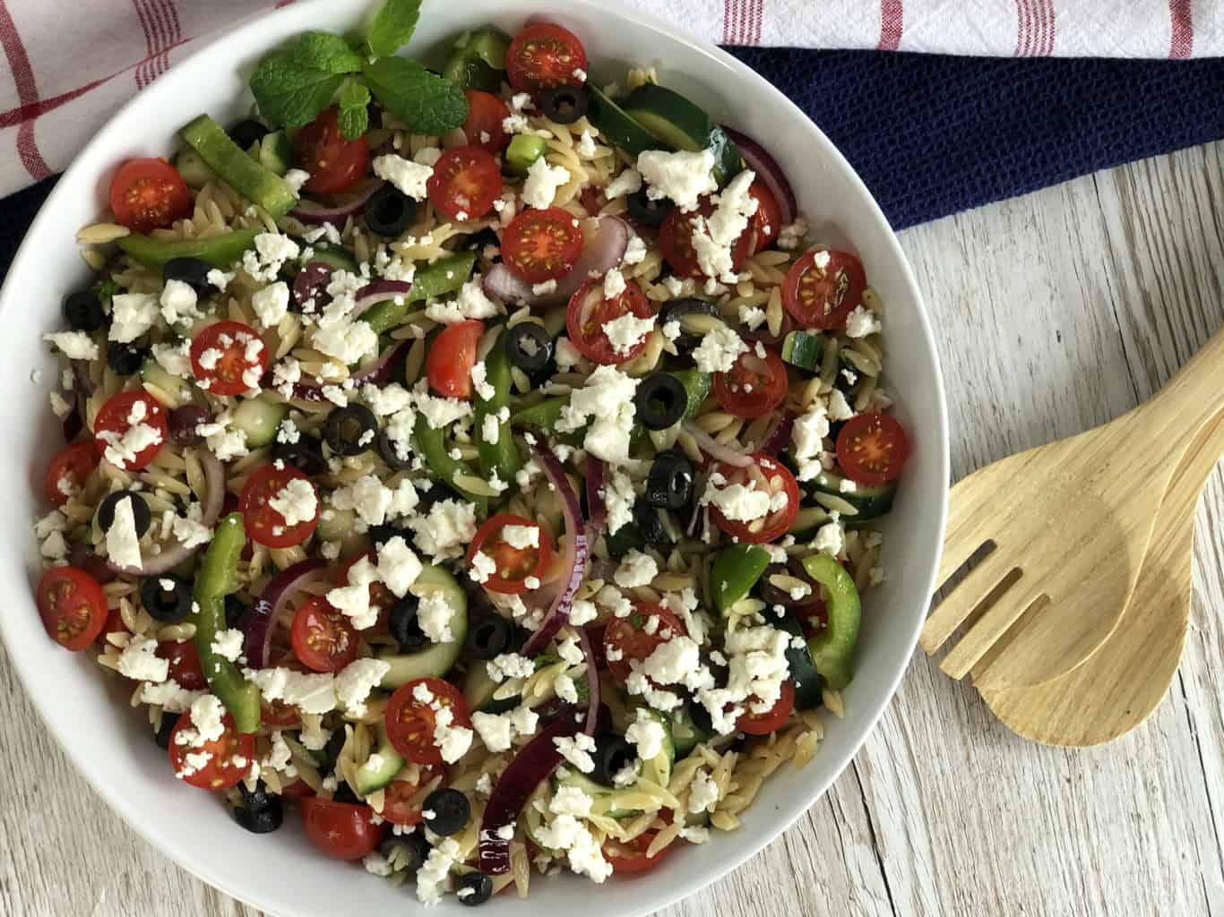 An overhead photograph of greek orzo salad and two wooden serving spoons