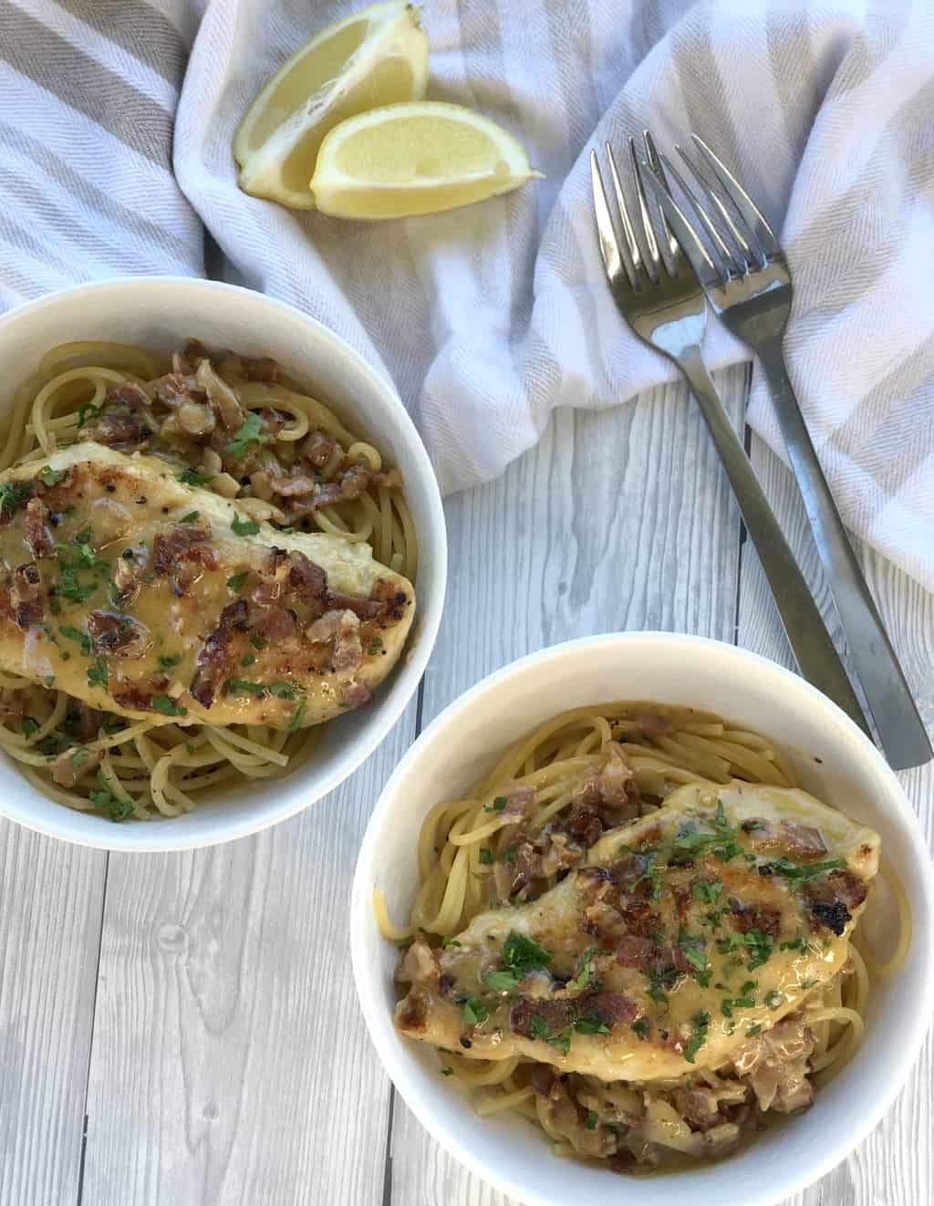 Two white bowls of spaghetti with a creamy bacon chicken breast placed on top, sprinkled with parsley