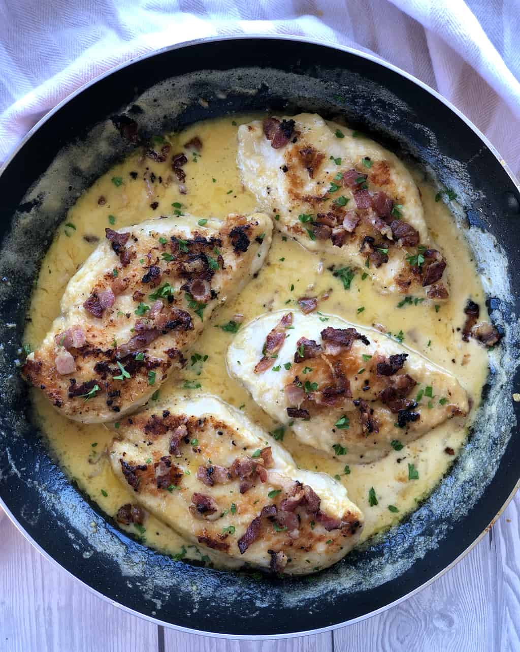 Overhead photograph of four chicken breasts in a creamy sauce with bacon bits 