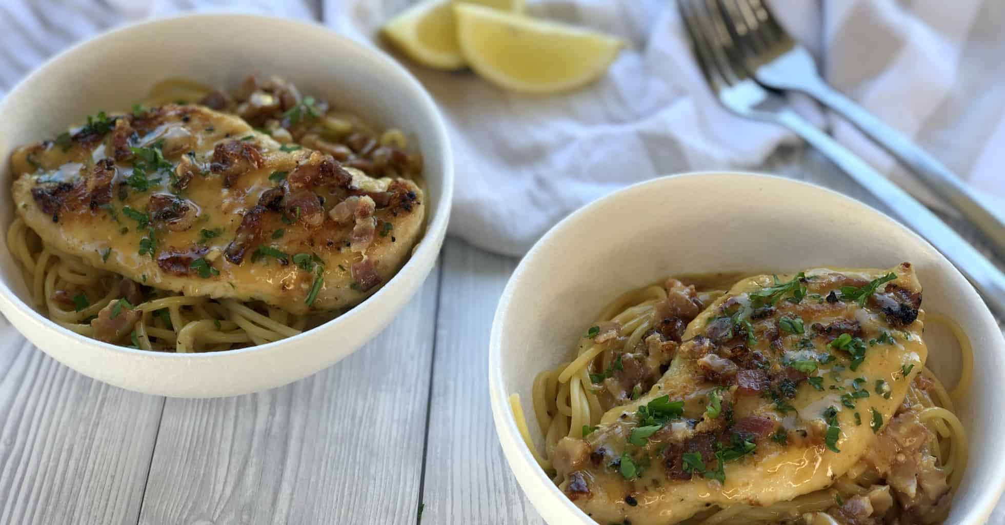 Two bowls of noodles with a chicken breast placed on top and creamy sauce 