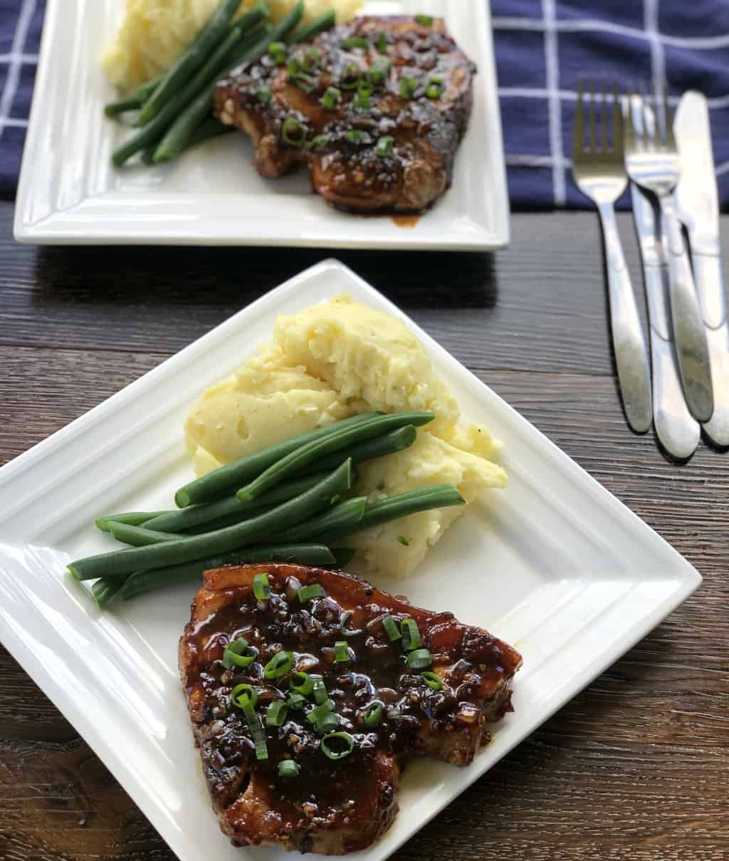 Two plates of pork chops with mashed potatoes and green beans and a glaze 