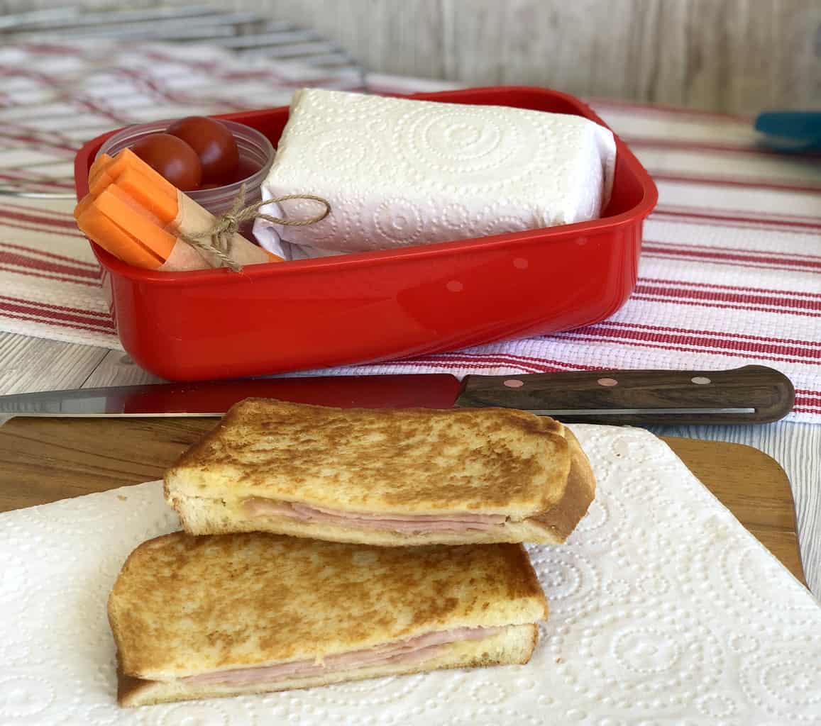 Cooled toasted sandwiches and a lunch box with wrapped sandwich and vegetables. 