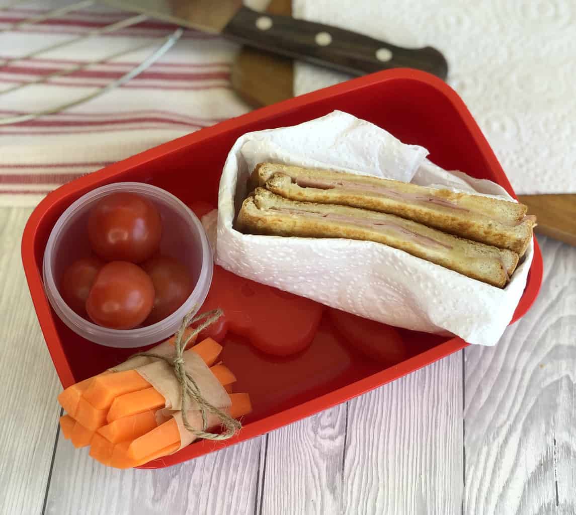 A red lunch box with a cooled toasted sandwiches and vegetbles 