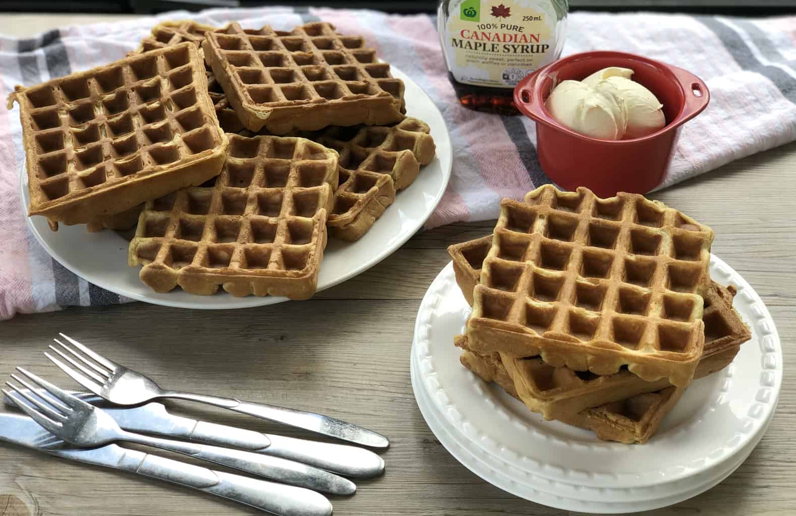 Plates of waffles with a bottle of Canadian maple syrup and a bowl of cream 