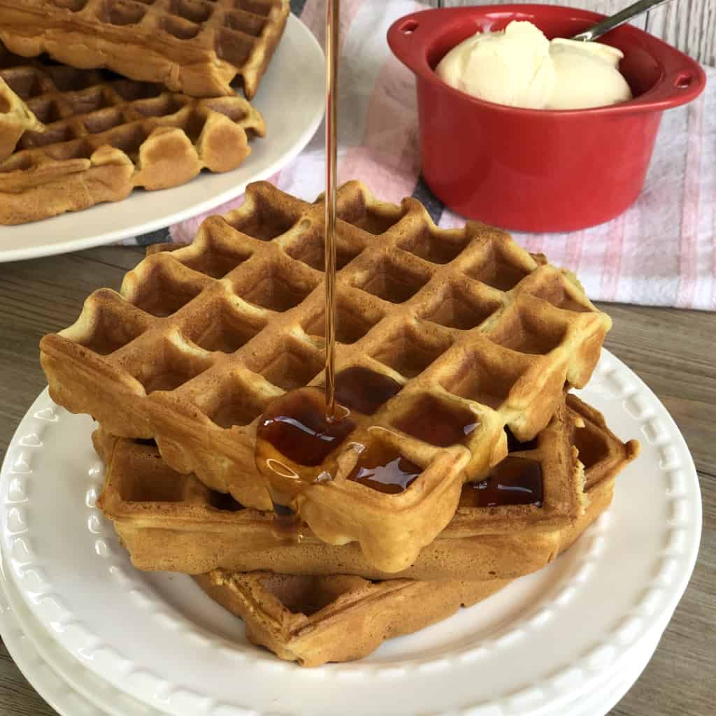 Plate of waffles with maple syrup pouring onto it and a bowl of cream 