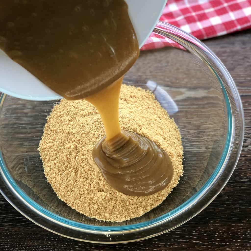 Butter and ginger mixture being poured into crushed biscuits 