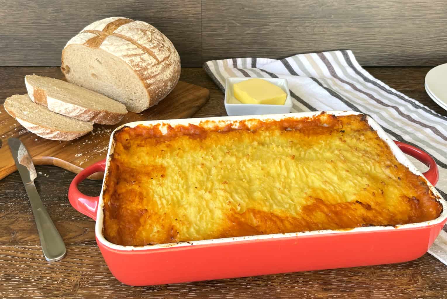 Large red dish with devilled sausage shepherds pie, crusty loaf of bread and butter 