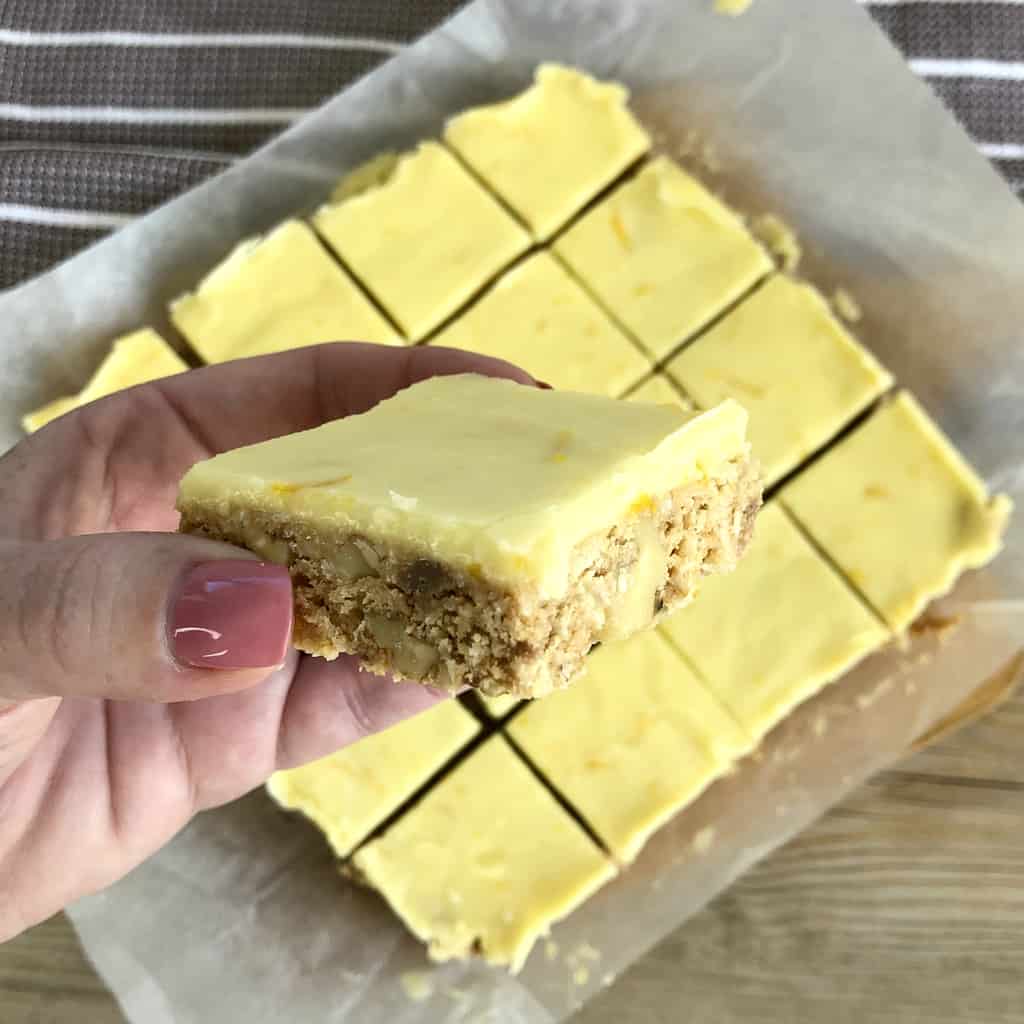 A hand holding a piece of no bake slice close to the camera where you can see the orange zest and walnuts