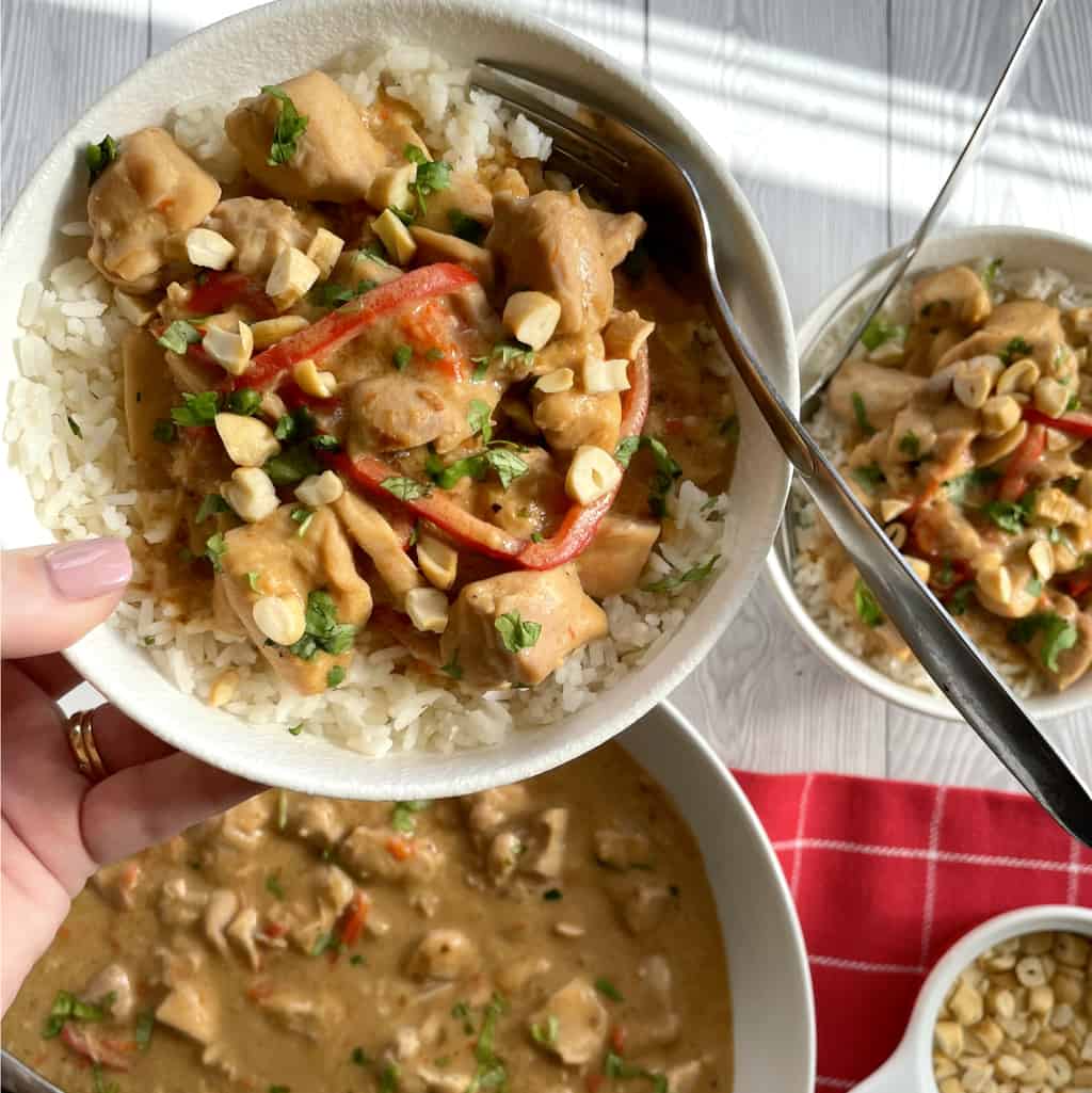 hand holding a bowl of satay chicken slow cooked served over rice 
