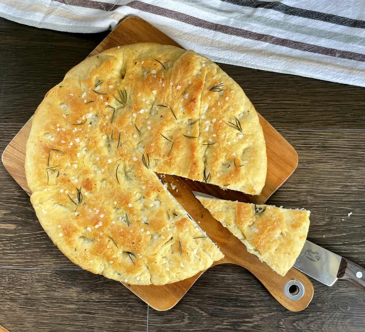 Overhead shot of golden brown focaccia with sea salt and rosemary with a triangle slice cut out