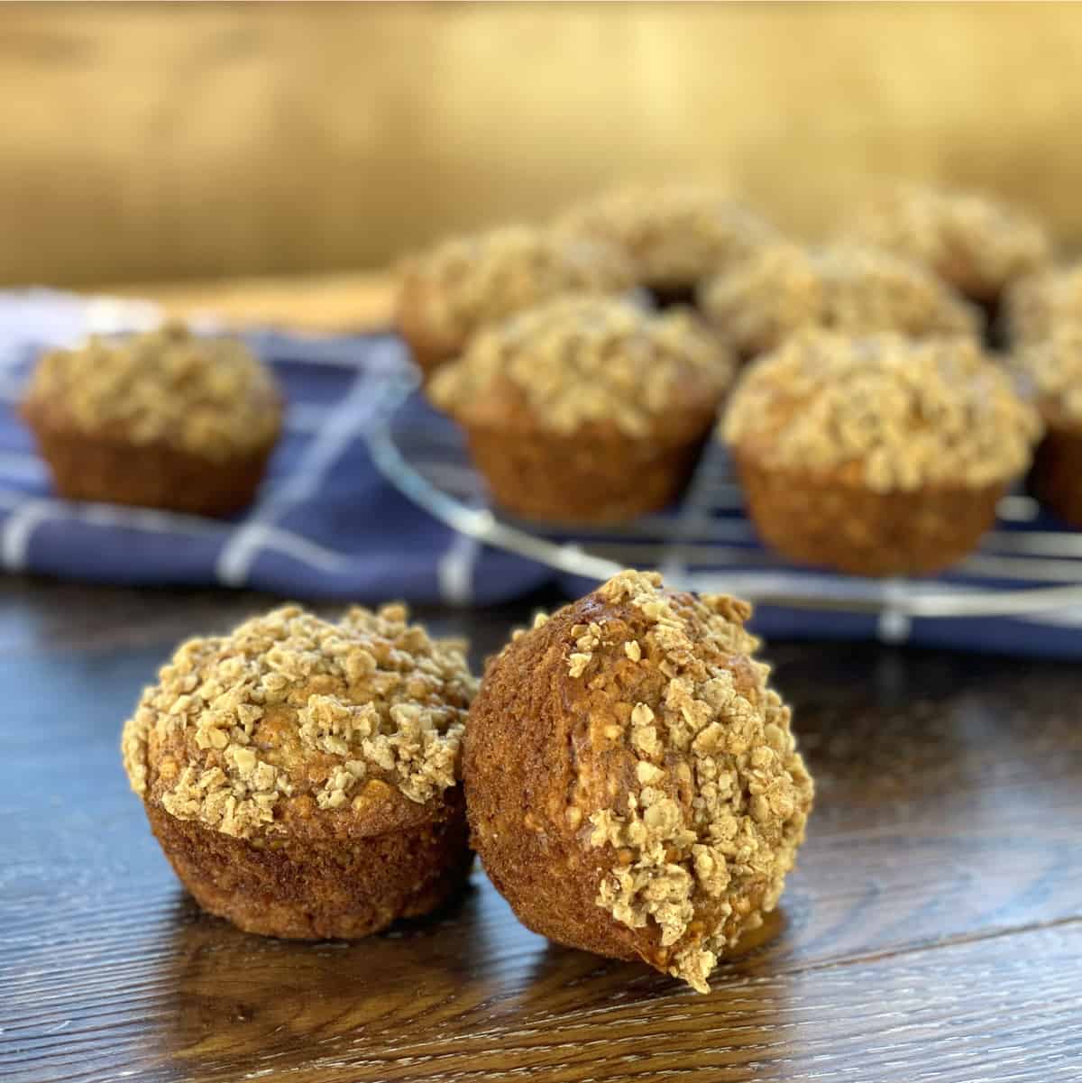 Close up photo of two banana oat muffins with a crunchy topping and more muffins in the bacckground 