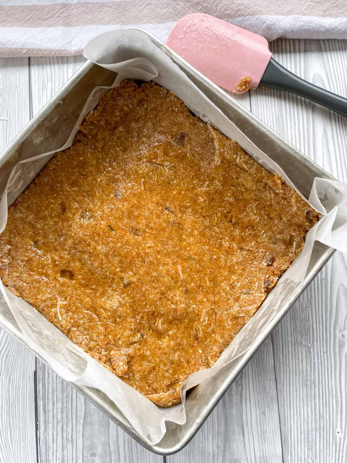 Pressed no bake slice in a baking tin with a pink and grey spatula 