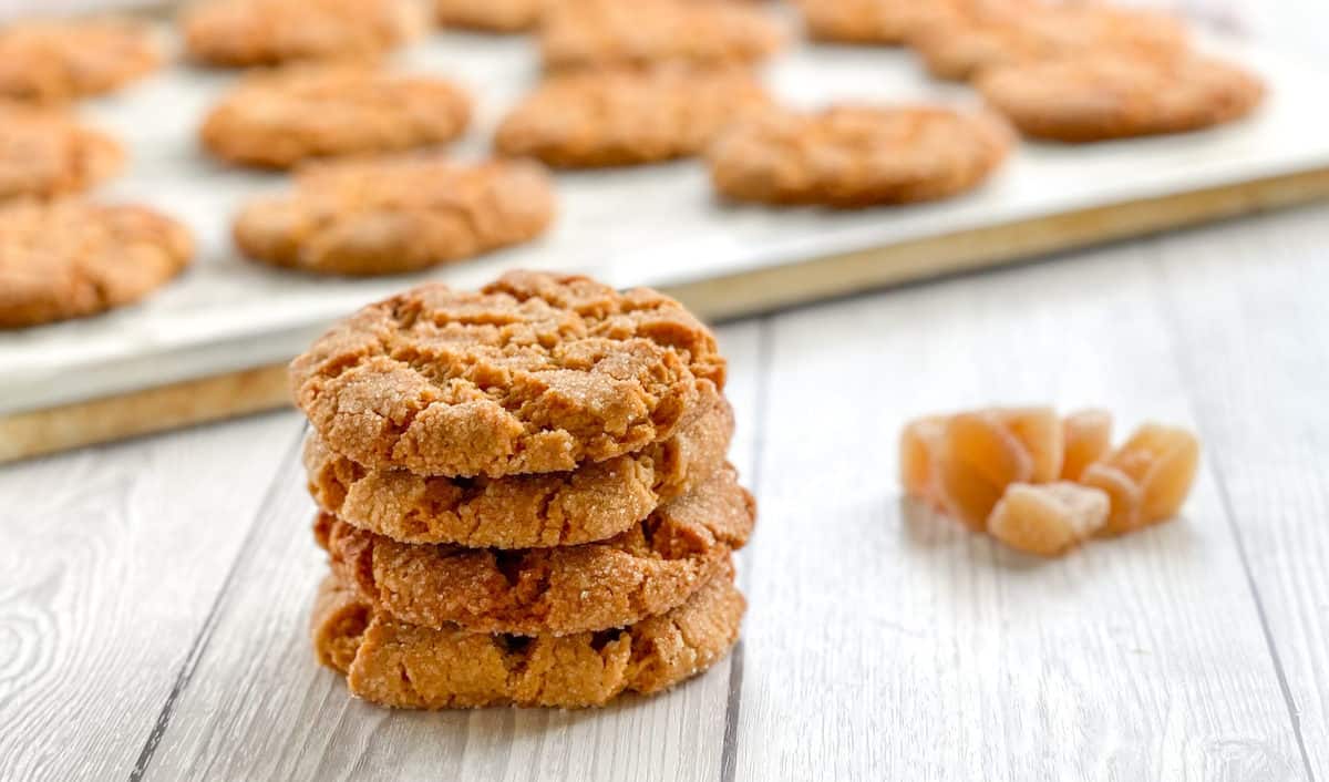 Pile of 4 ginger biscuits and a warm tray of biscuits in the background 