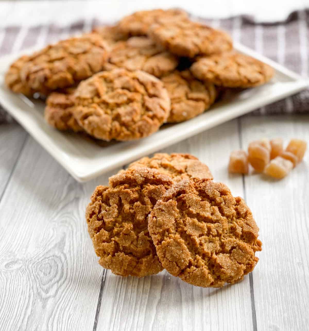 Plate of ginger biscuits with a selection of biscuits in the front and a pile of crystallized ginger. 