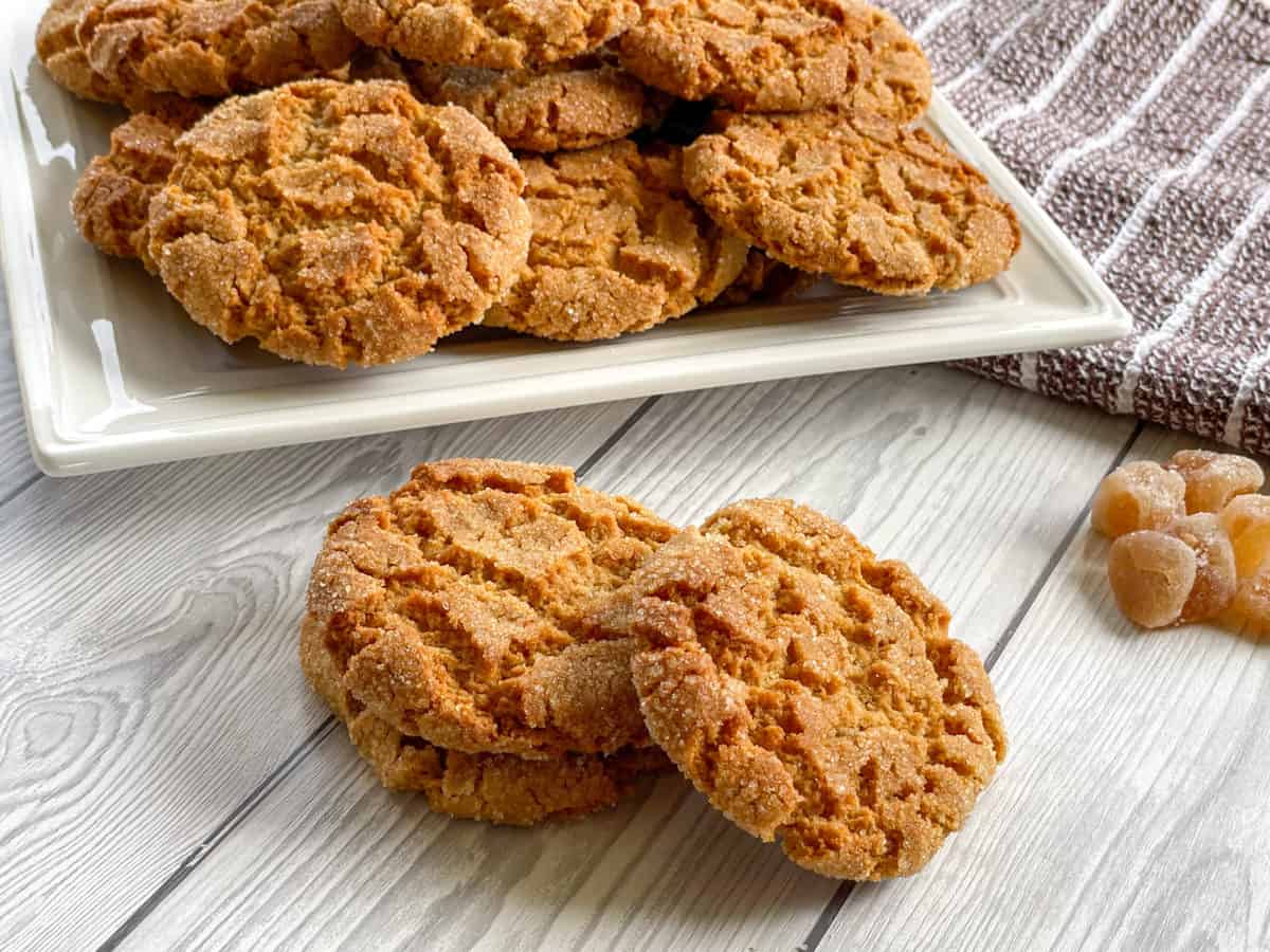 Pile of Chewy Ginger Biscuits with a tray of warm biscuits in the back