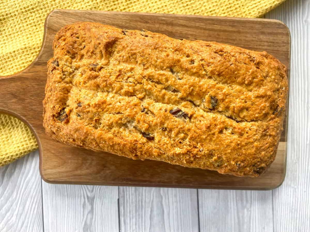 Freshly baked warm banana and date loaf on a wooden board with a yellow cloth 