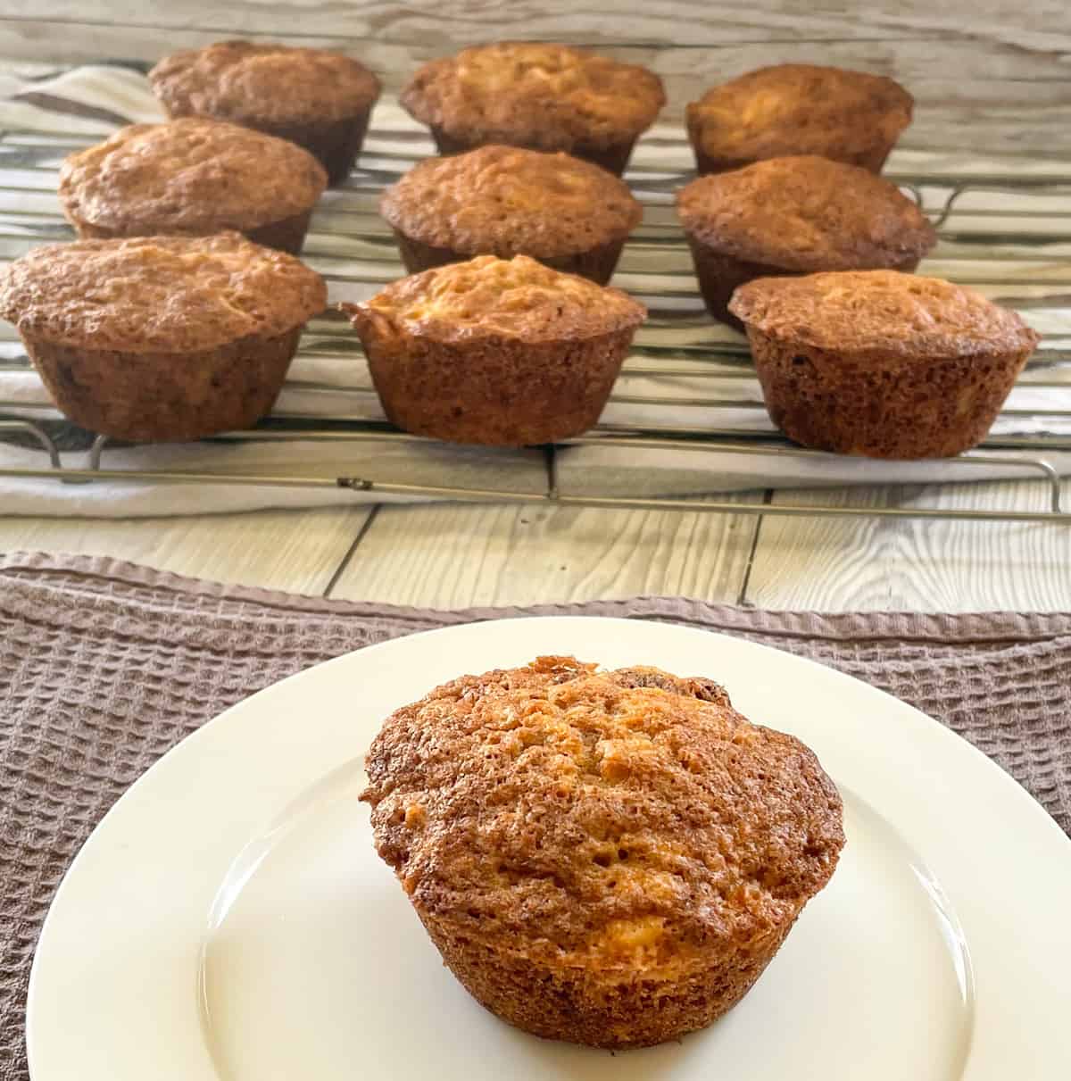 Muffins cooling on a wire rack and a plate with a single warm muffin 