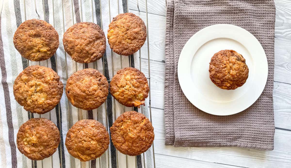 overhead photo of warm muffins on a wire rack and a white plate with a single carrot pineapple muffin 