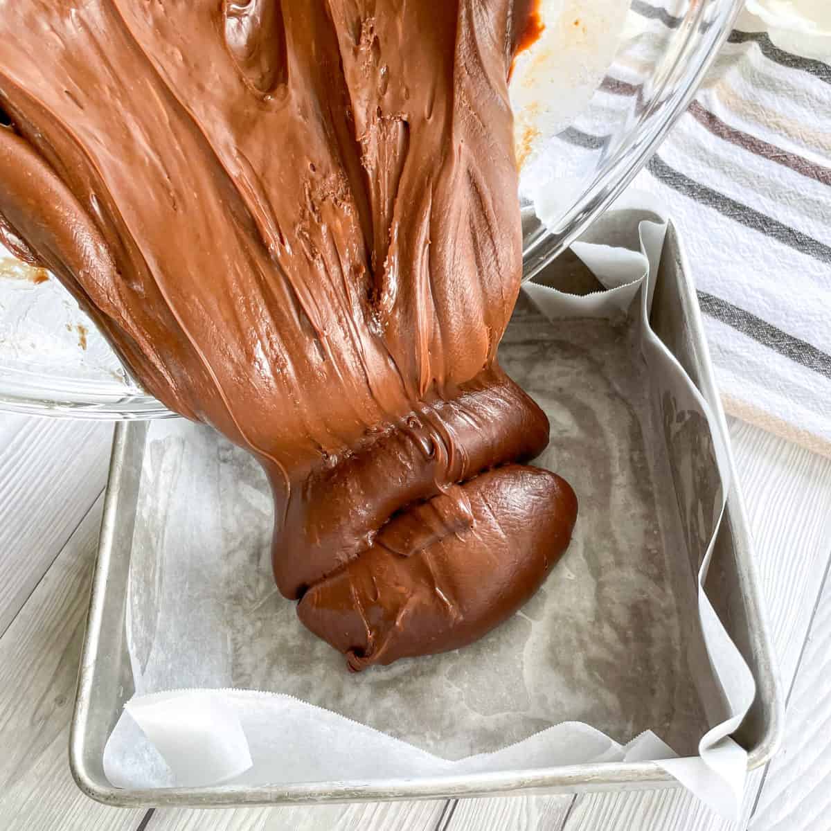 Pouring thick milk chocolate fudge into the prepared lined tin 