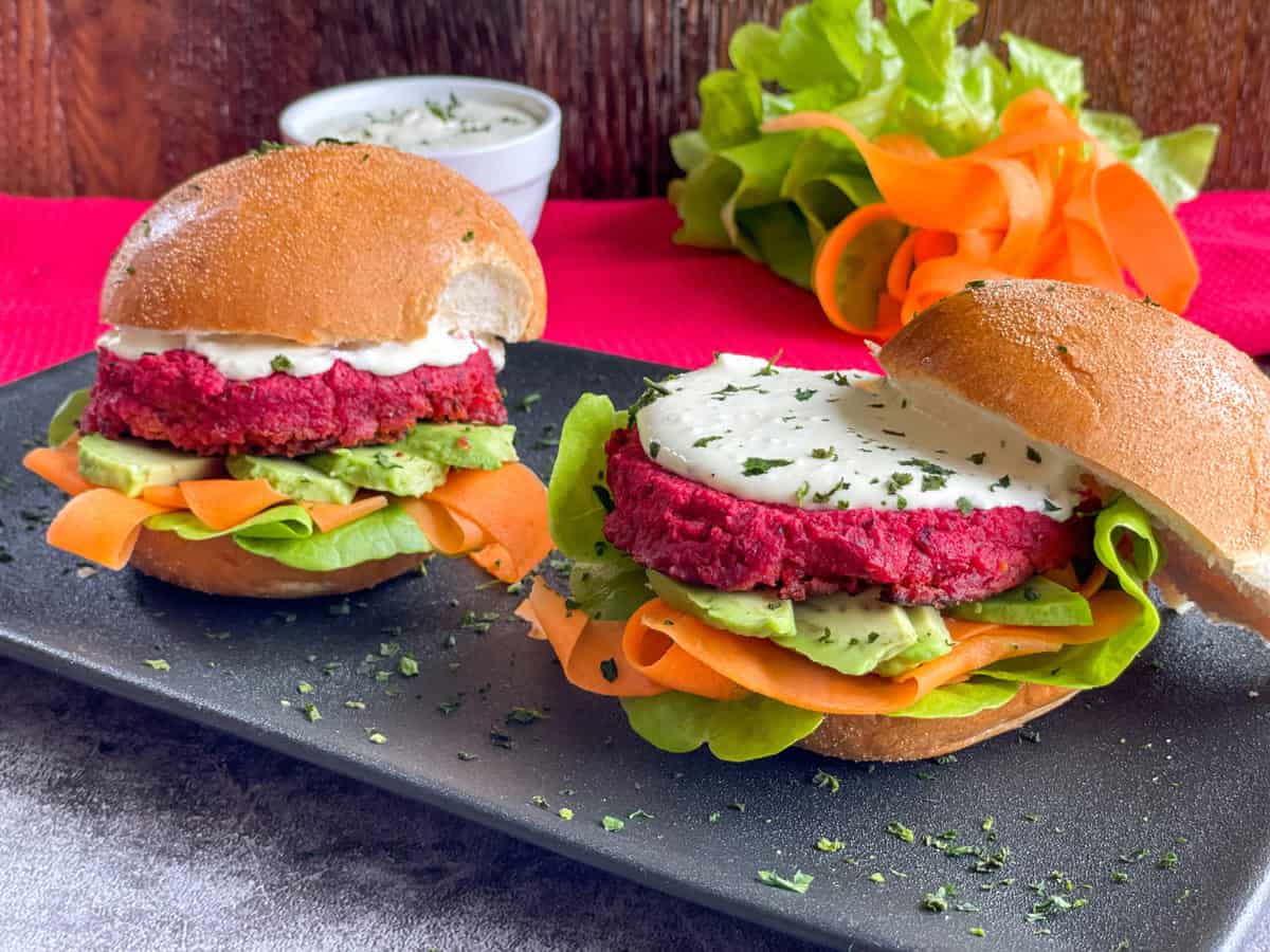 Beetroot burger patties on toasted buns with green and orange salad vegetables on a black plate