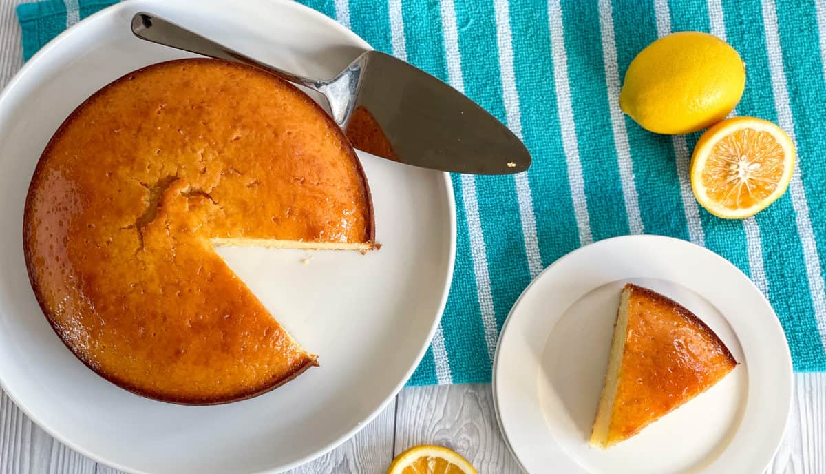 overhead photo of a lemon syrup cake with a slice separated onto a white plate