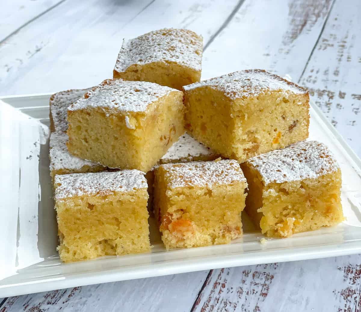 Plate of Apricot and White Chocolate slice on a white background dusted in icing sugar