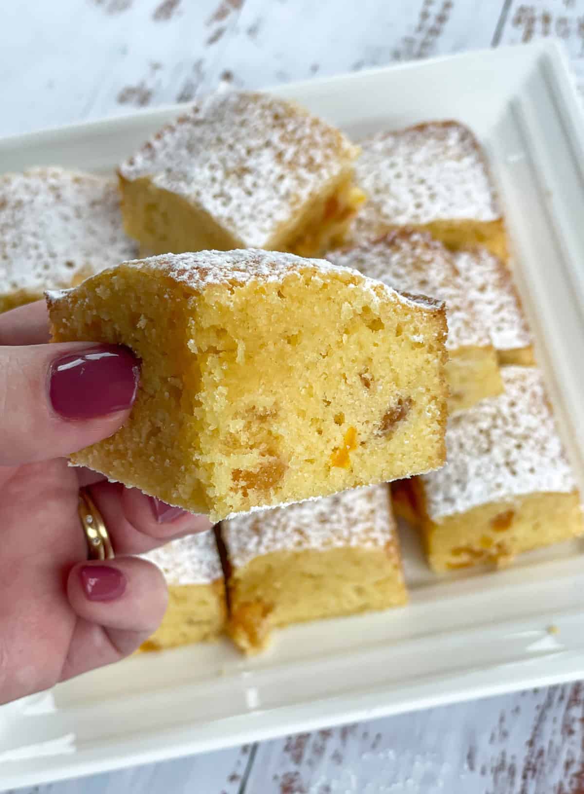 Hand holding a piece of apricot and white chocolate slice 