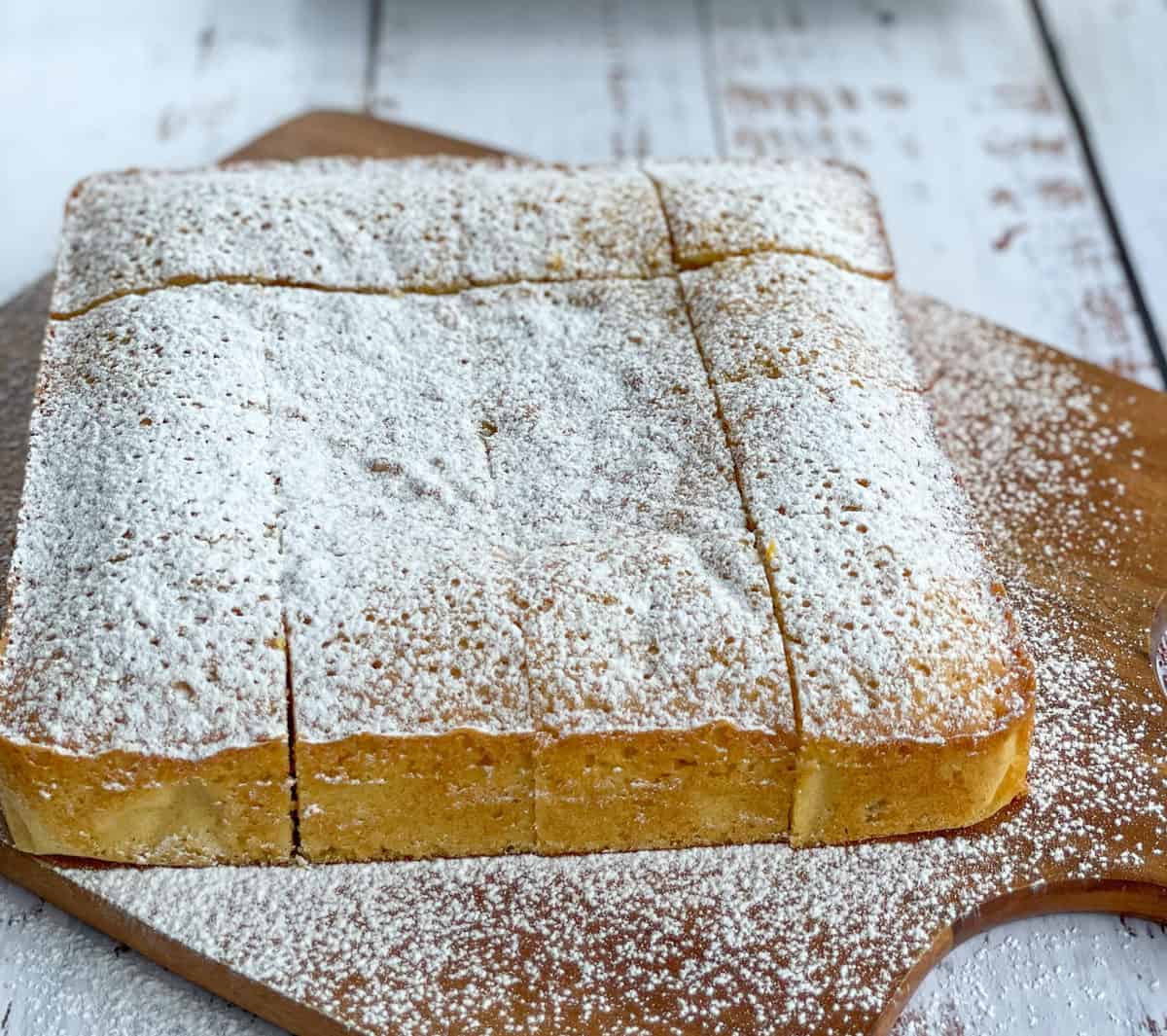 Icing sugar dusted white chocolate and apricot slice on a wooden chopping board 