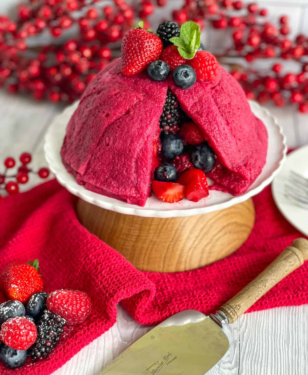 Summer berry pudding on a white serving dish surrounded by red berries. 