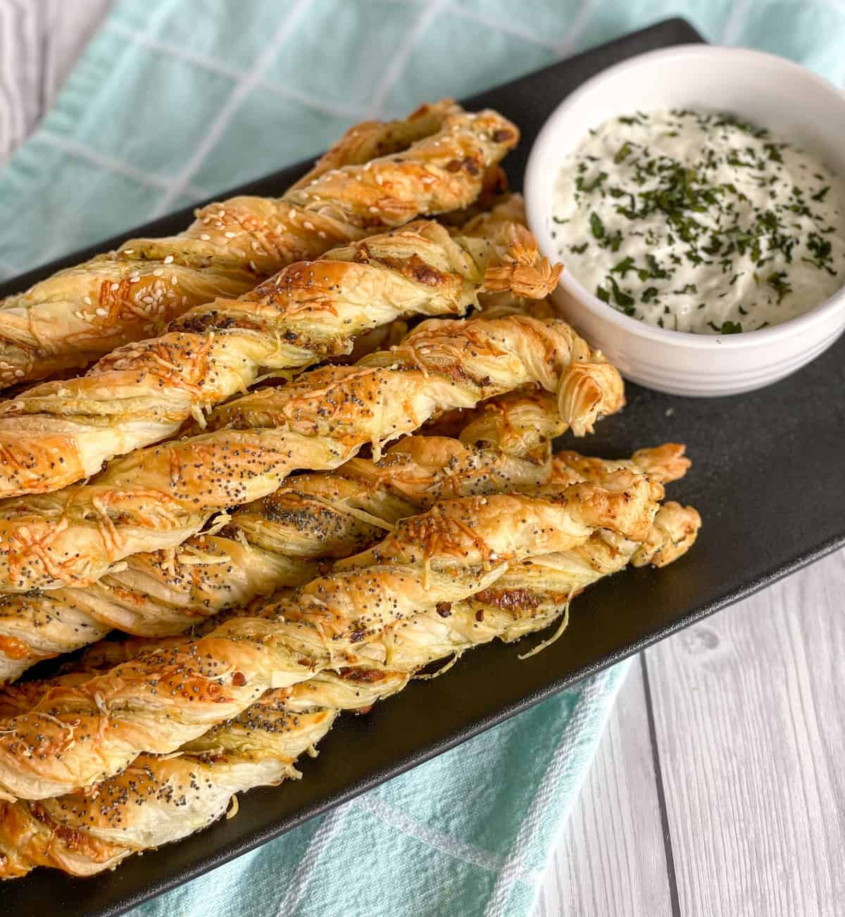 Pesto Pastry Twists on a black plate with a bowl of white cucumber yoghurt dip 