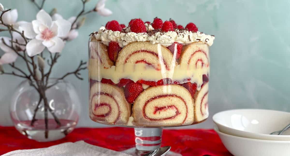 Large trifle in a glass bowl with a bowl of white magnolias and two white dessert bowls